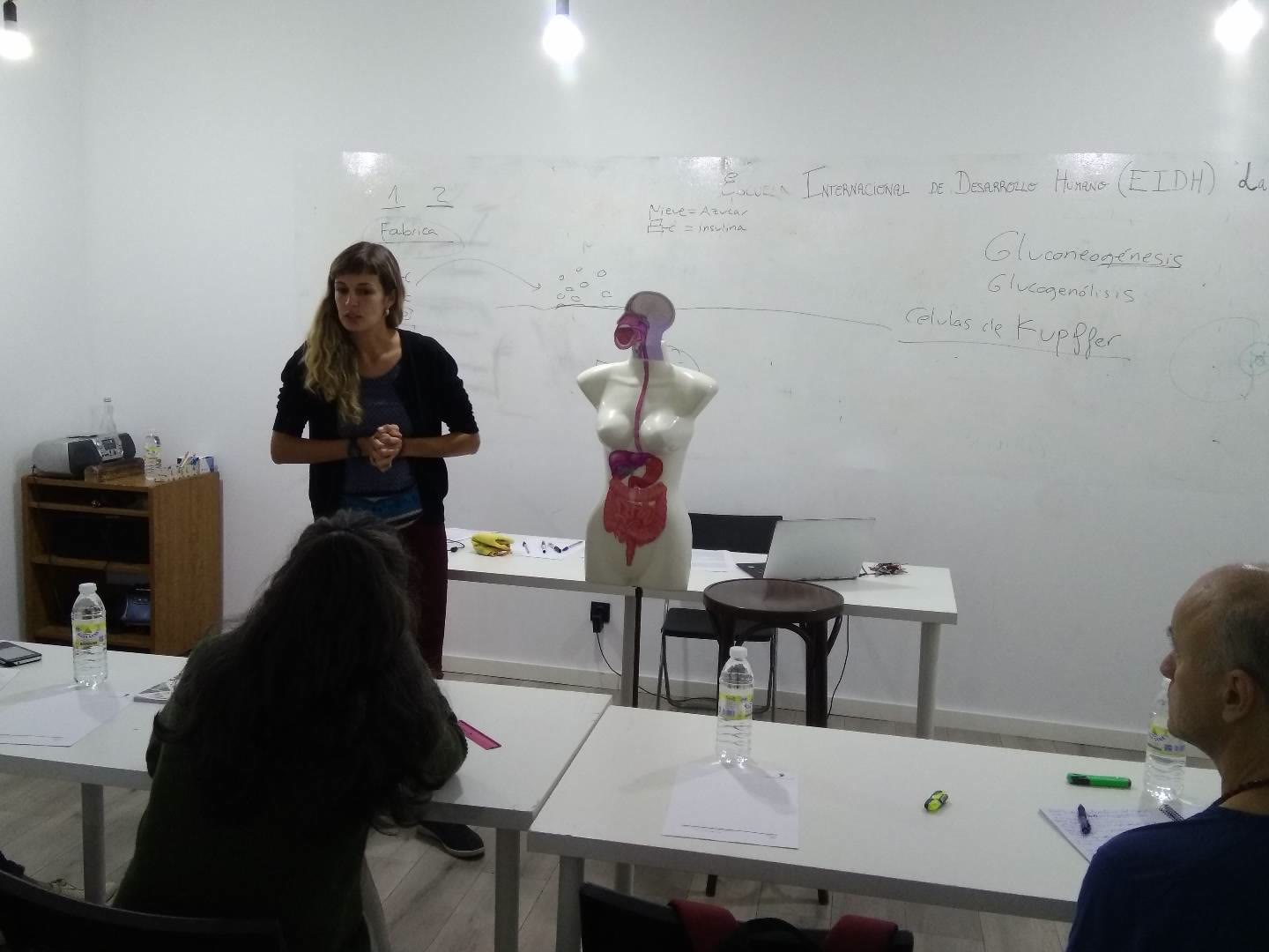 Profesora explica anatomía ante la pizarra con el alumnado en primer plano