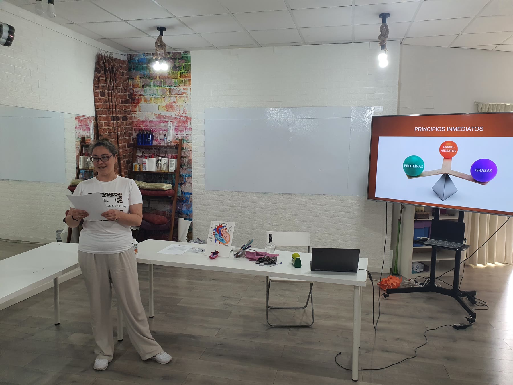 Profesora explicando nutrición junto a una gran pantalla